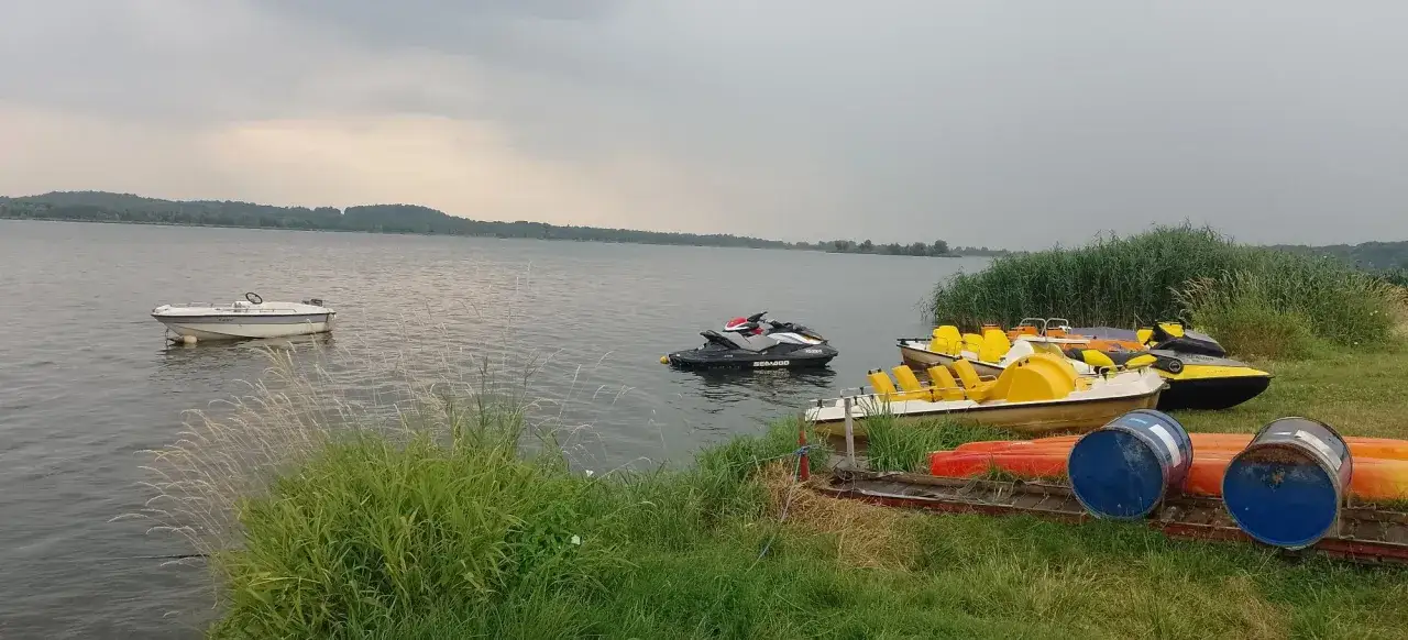 Jezioro Paczkowskie z ł&oacute;dkami, skuterami wodnymi i rowerami wodnymi na brzegu.