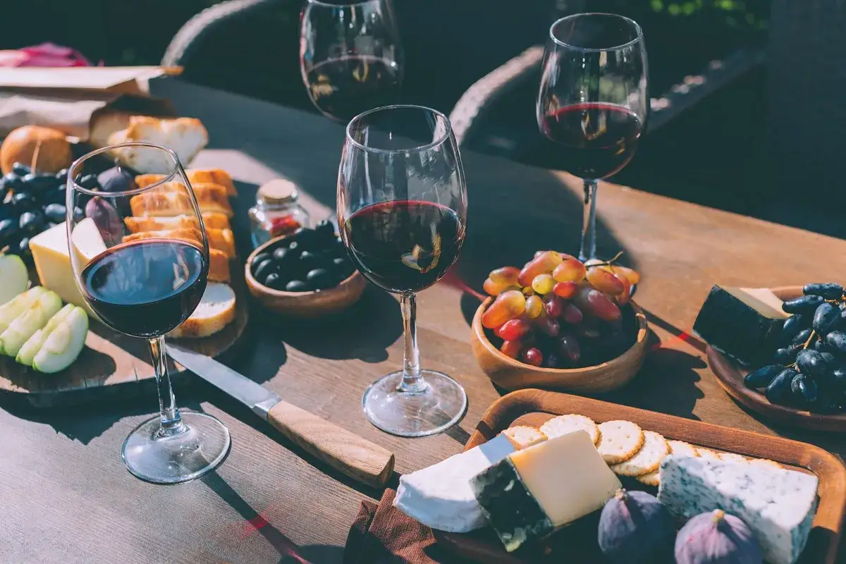 Degustacja merlot veneto: kieliszki z czerwonym winem, sery, winogrona, oliwki i pieczywo na drewnianym stole.