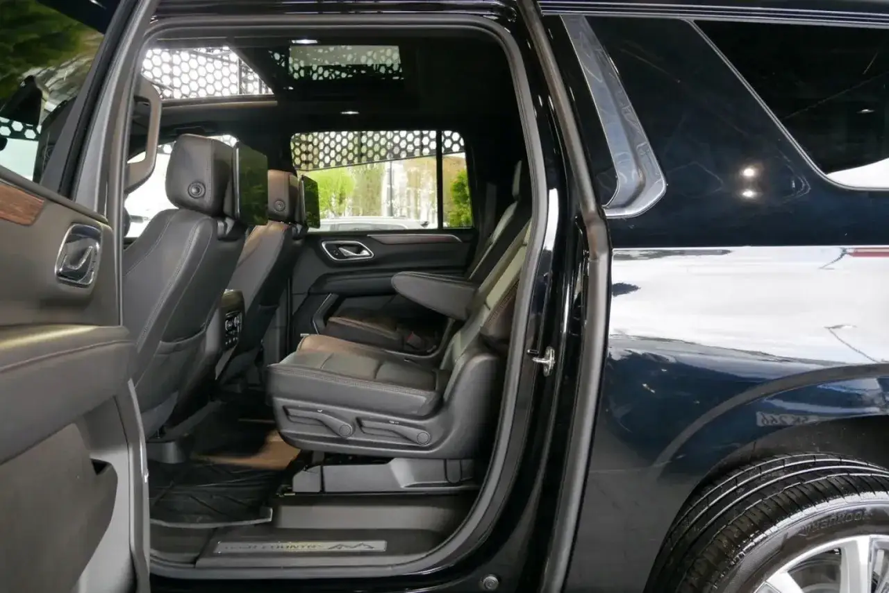 Wnętrze czarnego Chevrolet Suburban z czarnymi skórzanymi fotelami, ekranami dla pasażerów i panoramicznym dachem.