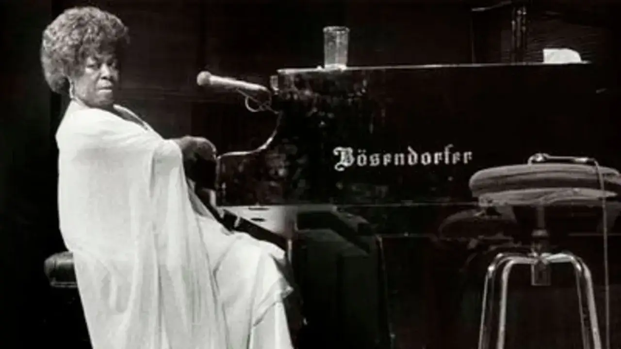 Dinah Washington, con su icónico peinado afro, sentada al piano Bösendorfer, lista para ofrecer una actuación inolvidable.