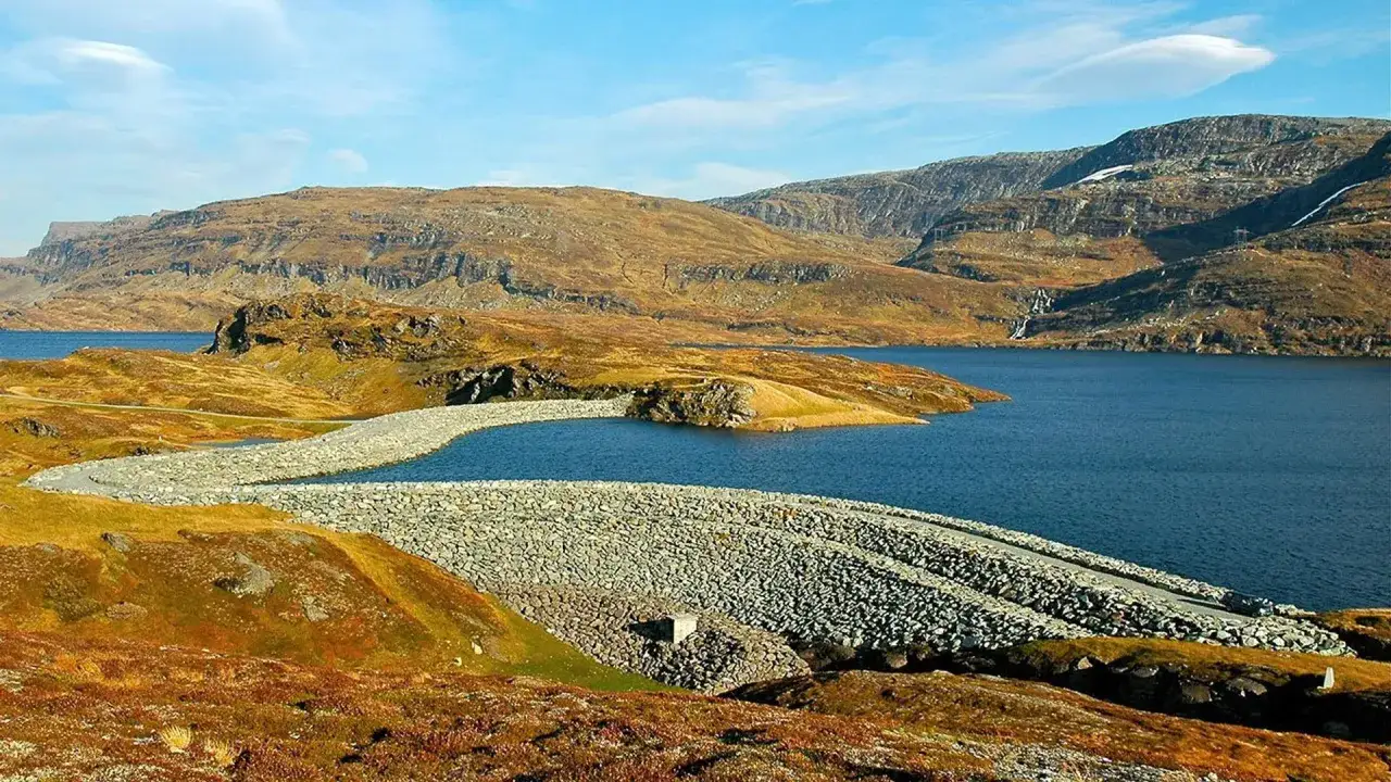 Staudamm in Norwegen, der die Kraft des Wassers für erneuerbare Energien nutzt. Die Landschaft ist von Bergen und einem tiefblauen See geprägt.