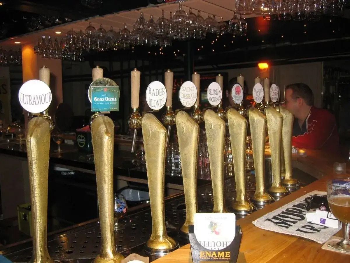 Rząd złotych kranów z piwem z kija w pubie. Widać nazwy piw: Ultramour, Bons Vœux, Rader Blonde, Saint Desbald Blonde, Delirium Nocturnum, Blanche des Neiges, Praïse Floris.
