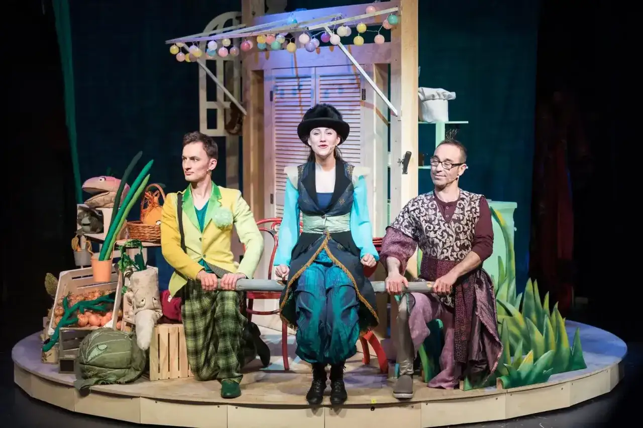 Aktorzy na scenie Teatru Gdynia w kolorowych strojach, przygotowani do kolejnych spektakli.