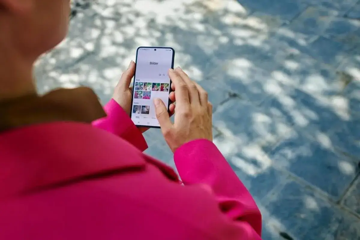 Osoba w różowej marynarce przegląda zdjęcia na telefonie, wśród nich widać kody orange.