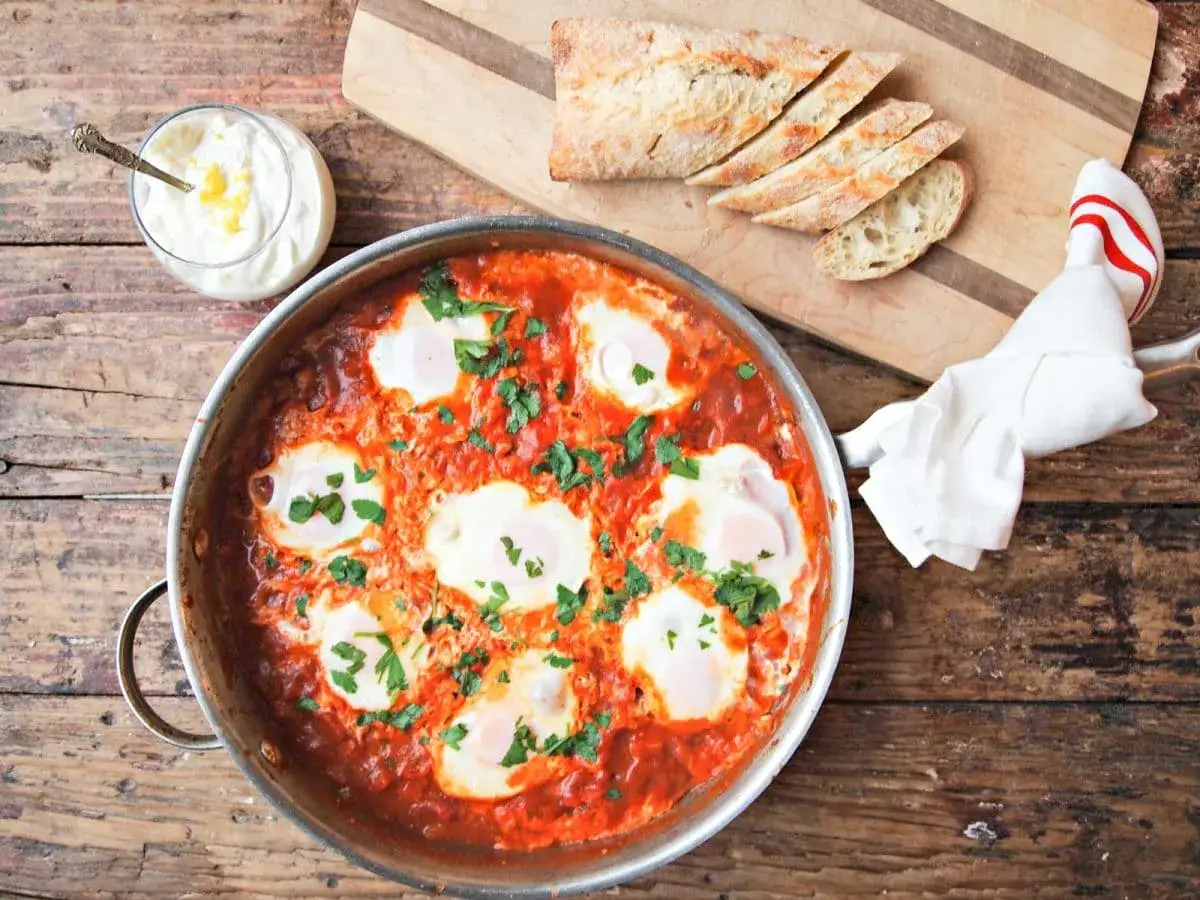 En smaklig shakshuka med &auml;gg i tomats&aring;s, serverad med br&ouml;d och en klick gr&auml;ddfil. Ett perfekt shakshuka recept f&ouml;r helgfrukosten.