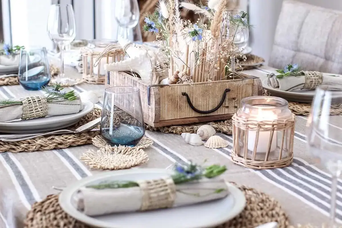 A modern everyday dining table decor with a coastal theme. Woven placemats, blue glasses, and seashell accents create a relaxed, beachy vibe.