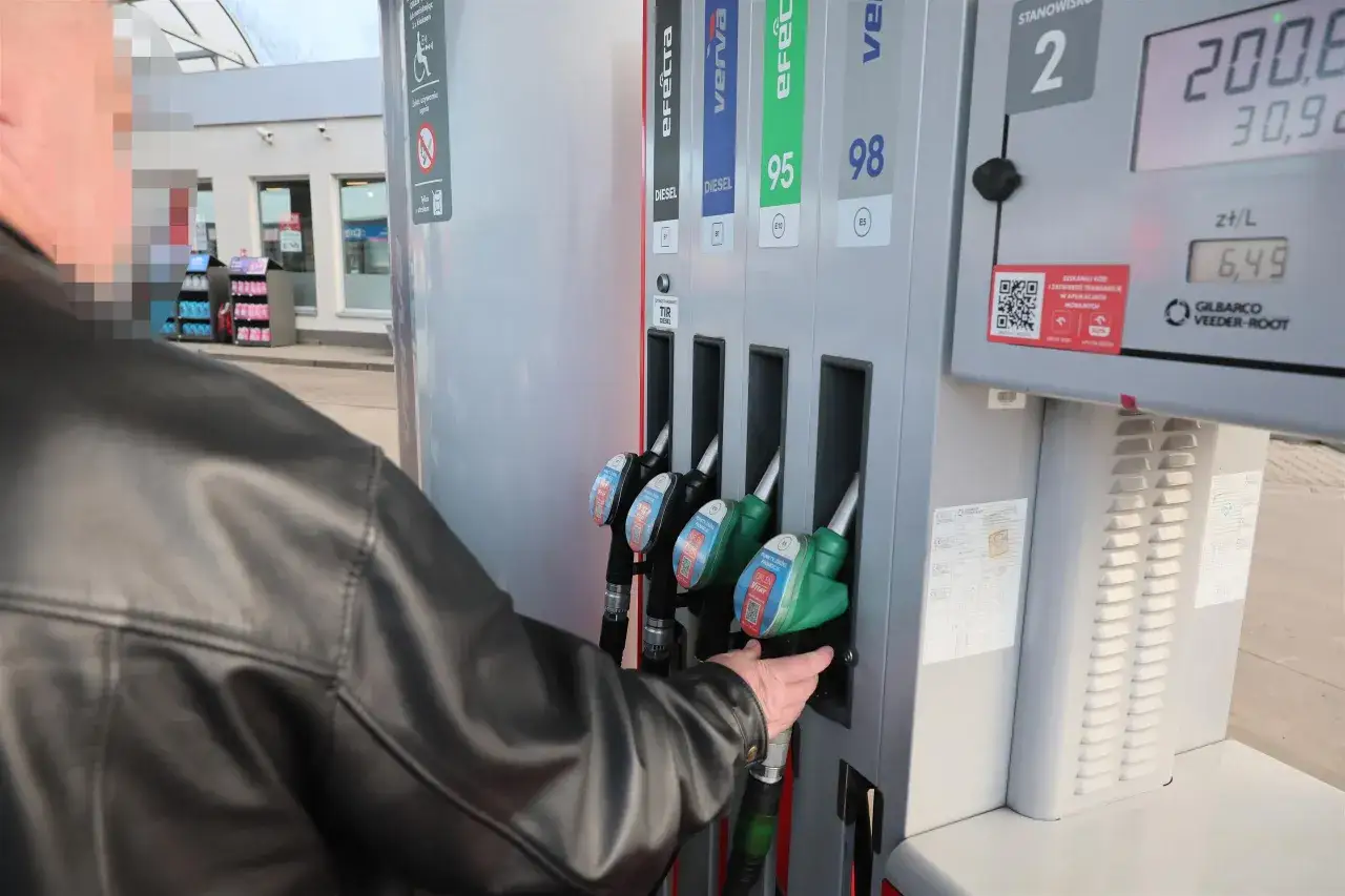 Mężczyzna w czarnej kurtce sięga po dystrybutor z napisem