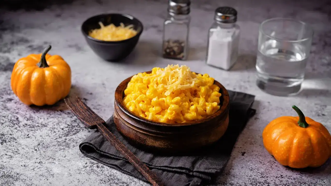 Un invitante piatto di pasta e zucca alla napoletana, guarnito con formaggio grattugiato, accanto a piccole zucche arancioni.