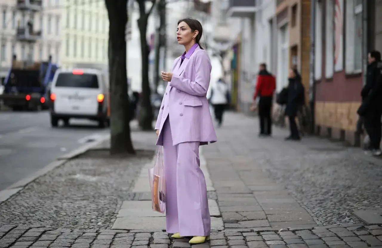 Elegancka kobieta w garniturze w kolorze liliowym, stojąca na brukowanym chodniku.