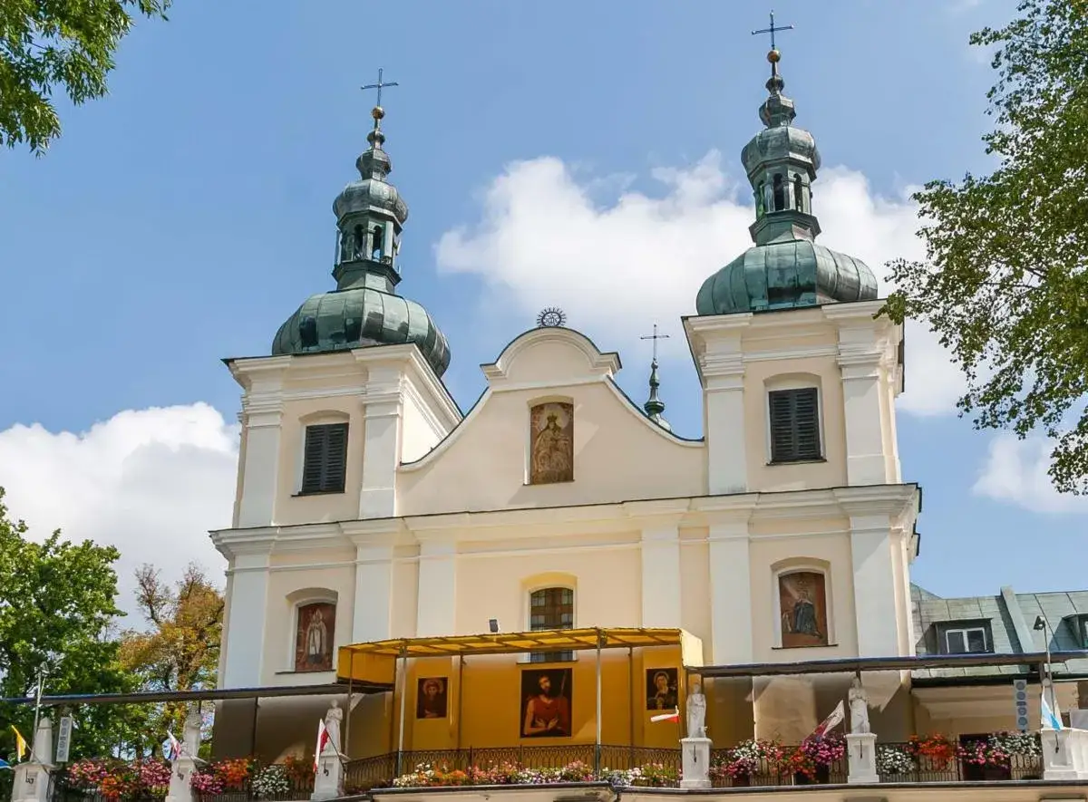 Kalwaria Pacławska dróżki: barokowa bazylika z dwiema wieżami, ozdobiona obrazami i kwiatami, pod błękitnym niebem.