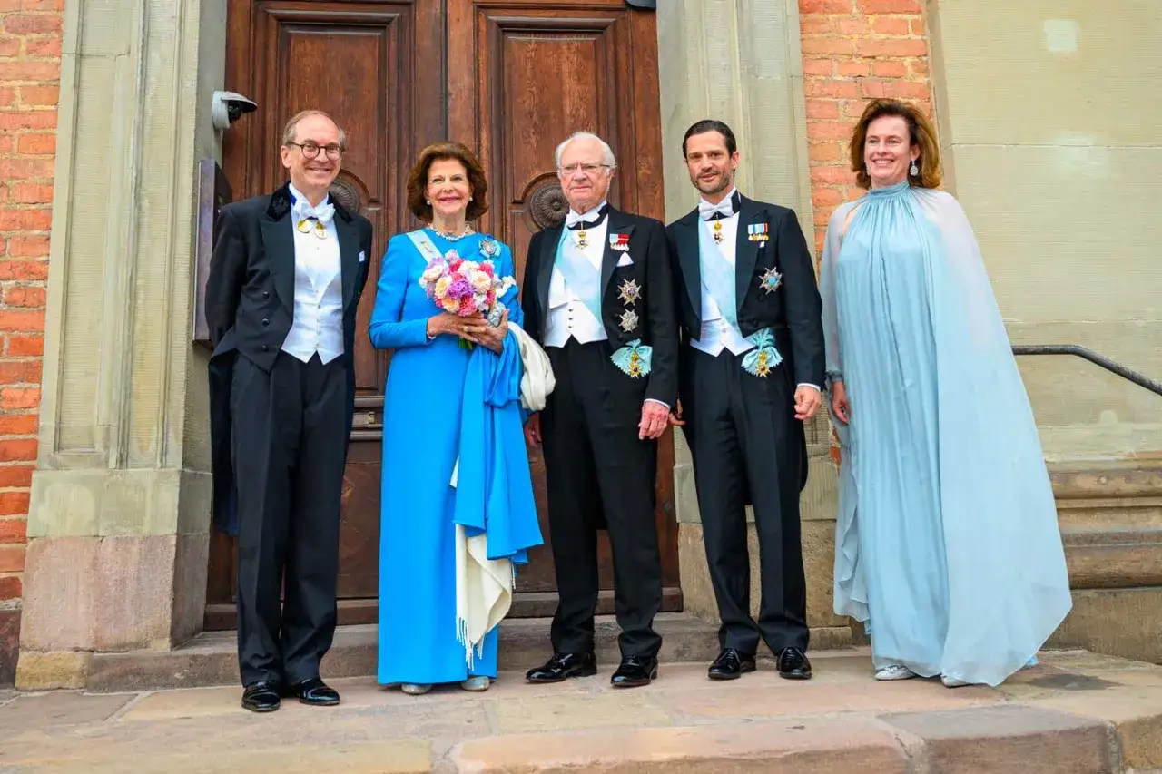 La famille de Sparre, élégamment vêtue, pose devant une porte en bois. La reine Silvia porte une robe bleue et tient un bouquet.