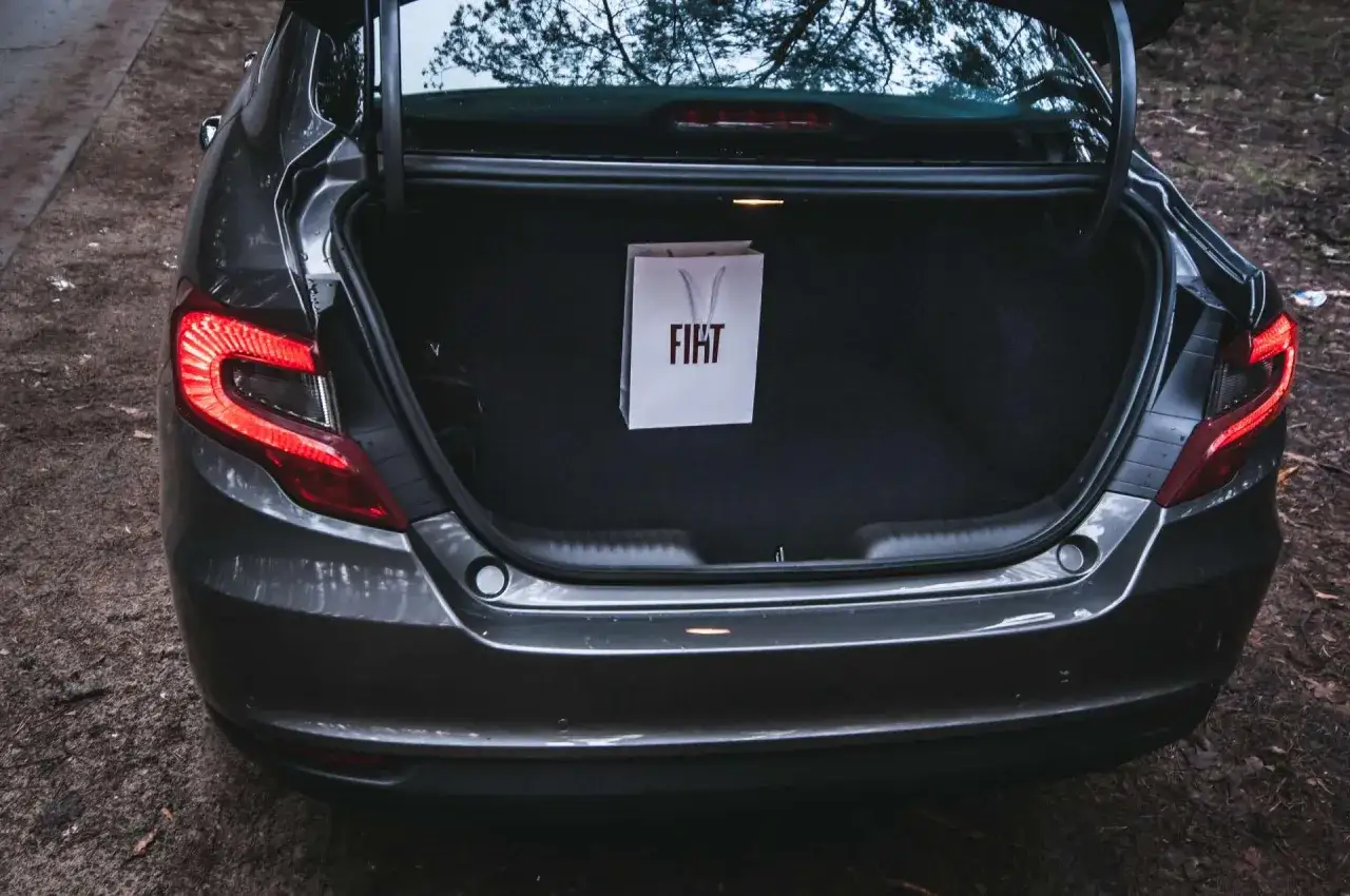Szary fiat sedan z otwartym bagażnikiem, w którym wisi biała torba z logo FIAT.