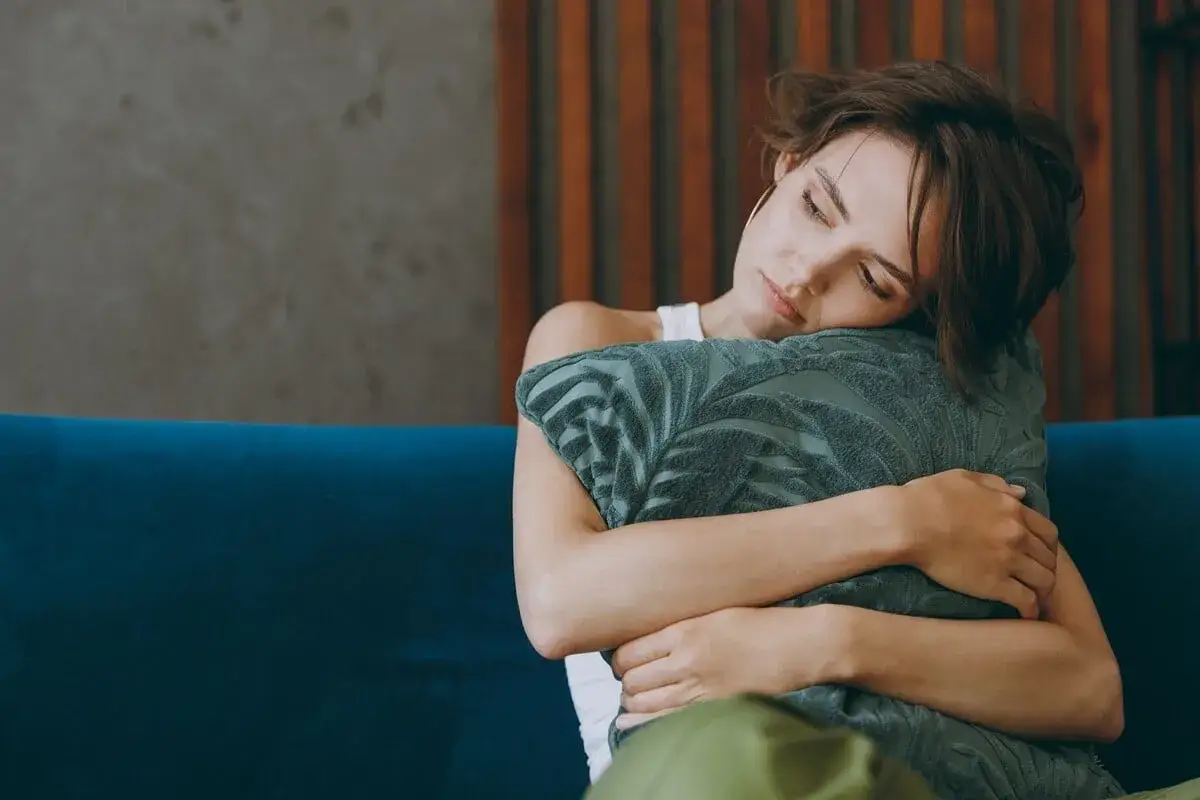 Une femme étreint un coussin, le visage appuyé dessus, le regard perdu. Elle cherche du réconfort, une aide pour savoir comment réagir quand un homme vous quitte.