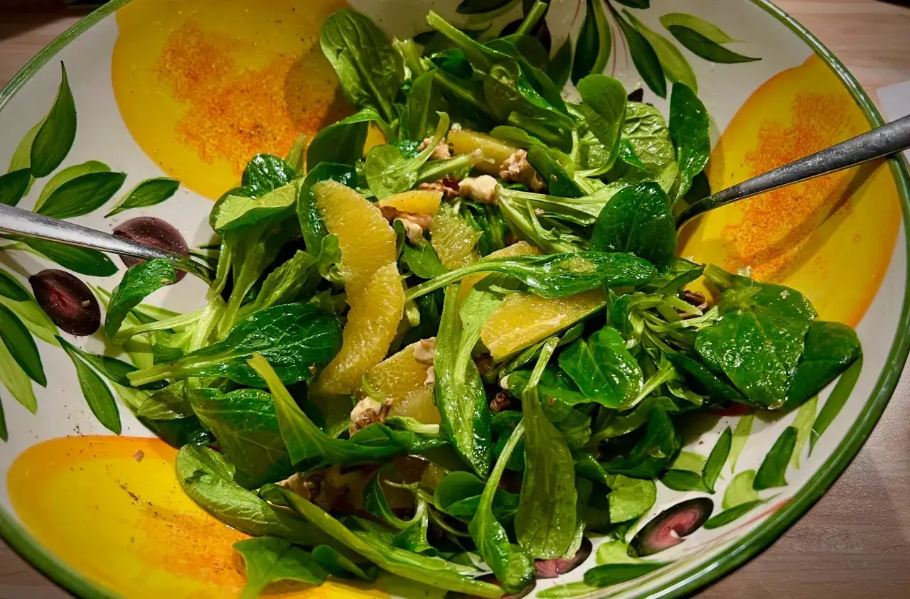 Frischer Feldsalat mit saftigen Orangenstücken und Nüssen in einer bunten Schüssel.