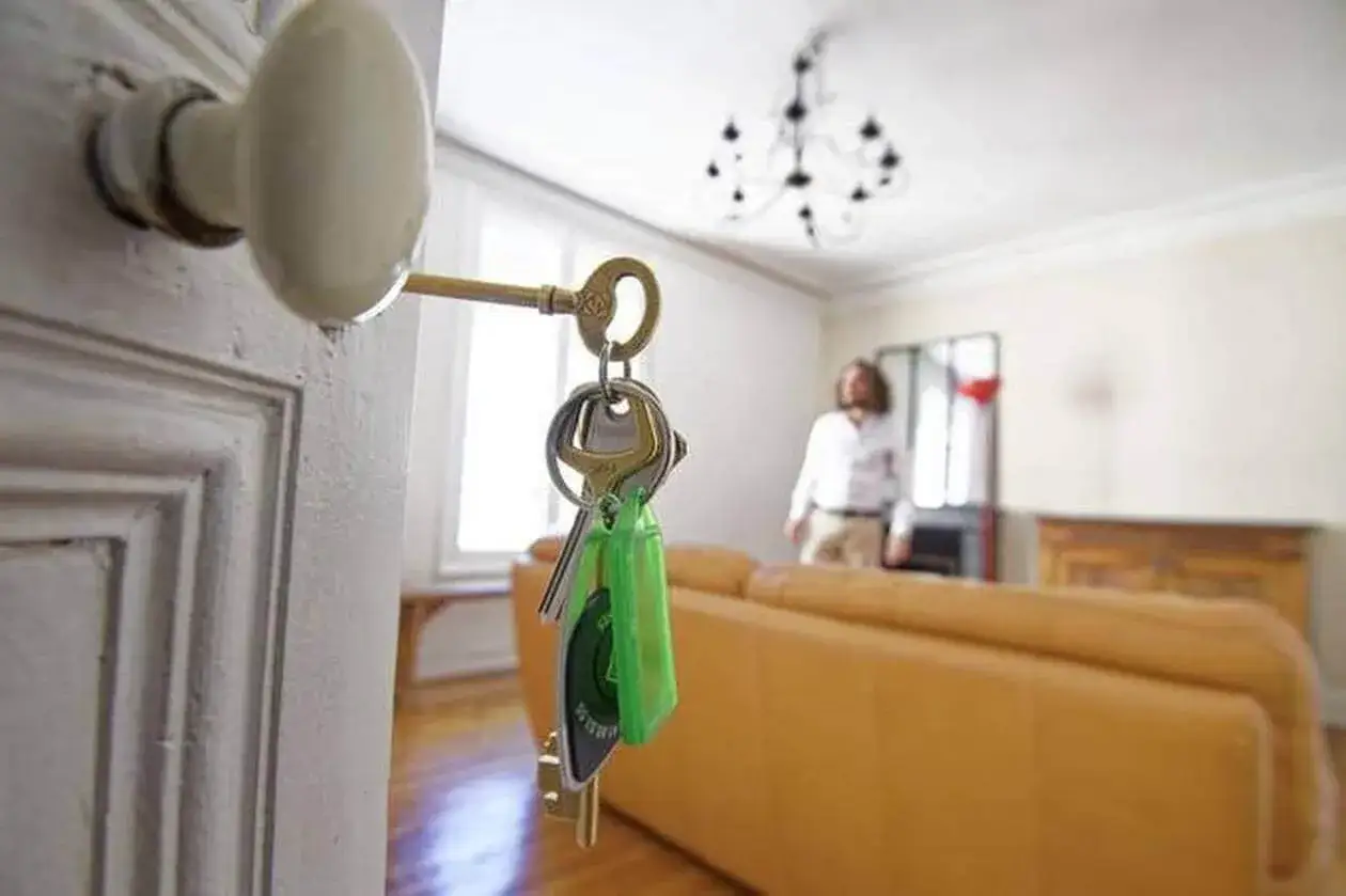 Clés d'un appartement, peut-être une arnaque location appartement ? Un homme flou attend derrière un canapé.
