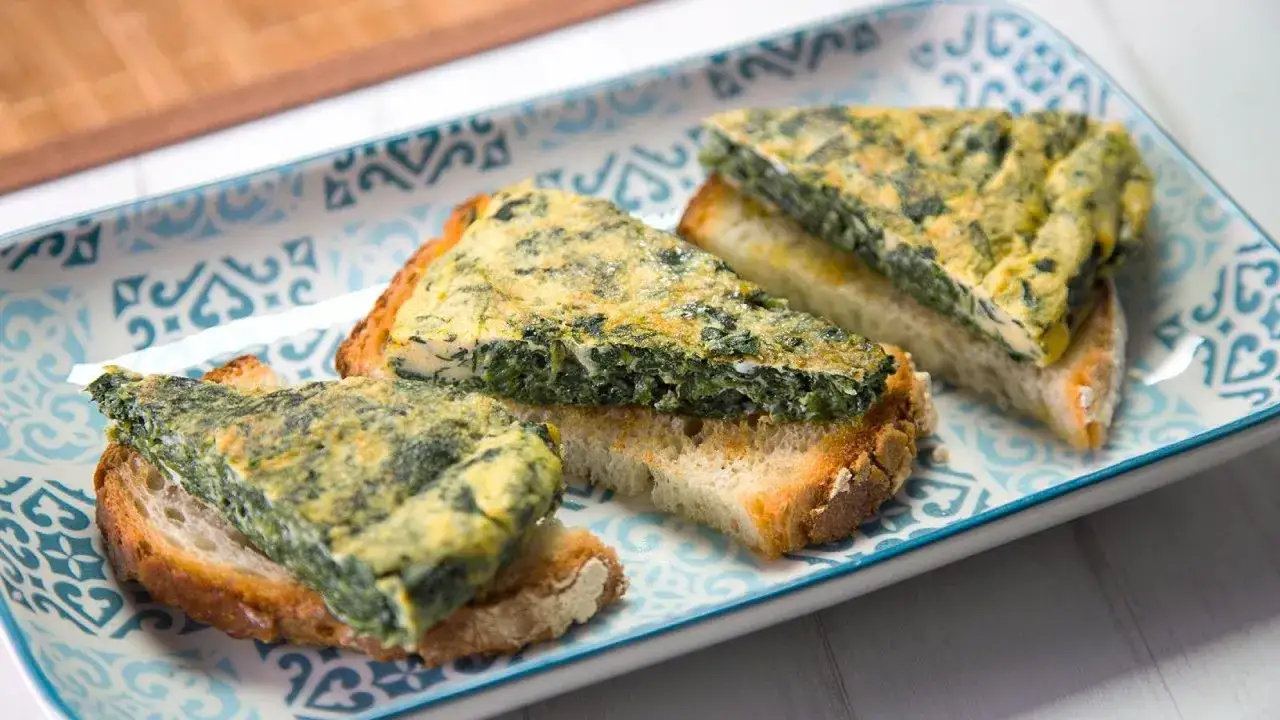 Rebanadas de pan tostado con una generosa porción de tortilla de espinacas encima, servidas en un plato decorado.
