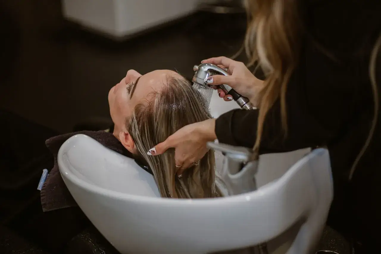 Una peluquera enjuaga el cabello de una clienta en un lavacabezas. Descubre los secretos de agua de esta peluquería para un cabello radiante.