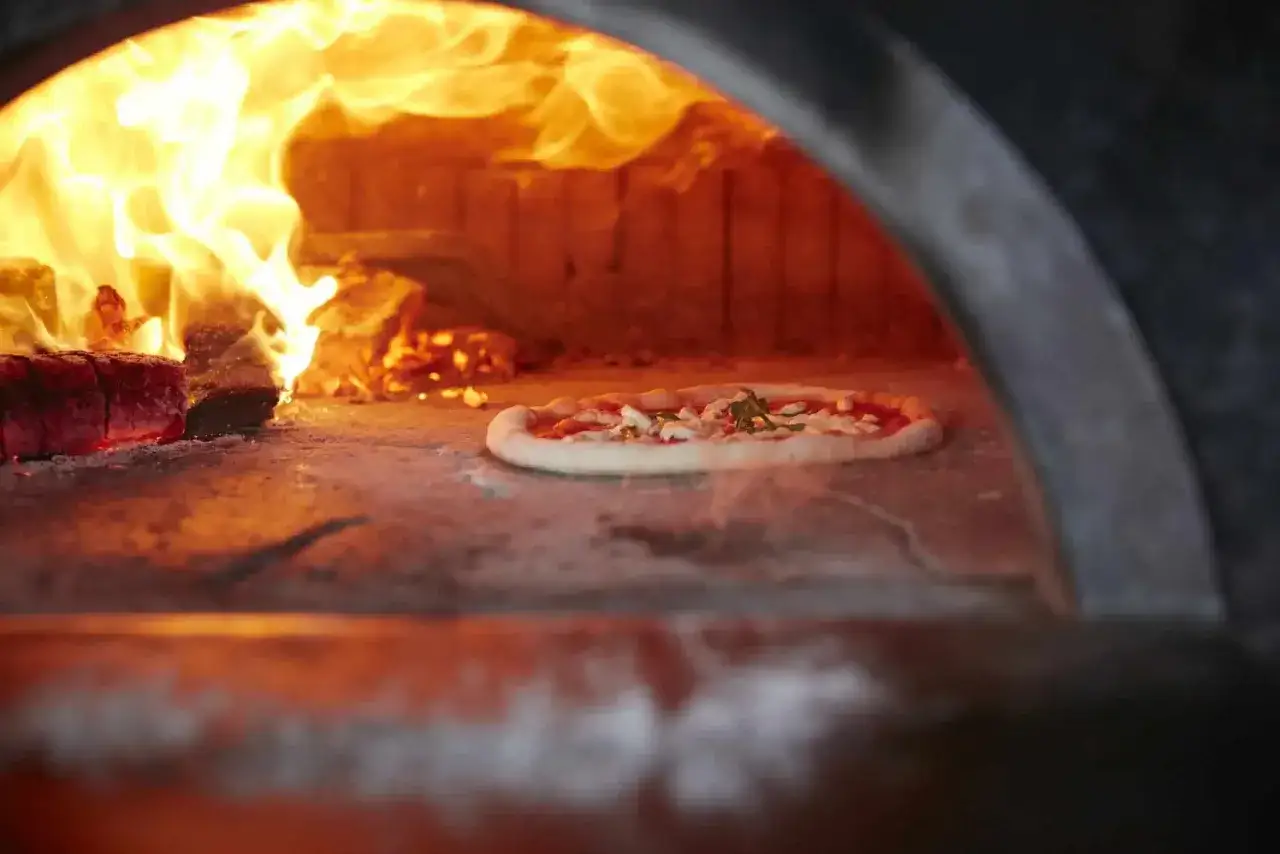 Eine neapel pizza b&auml;ckt im Holzofen, umgeben von lodernden Flammen.
