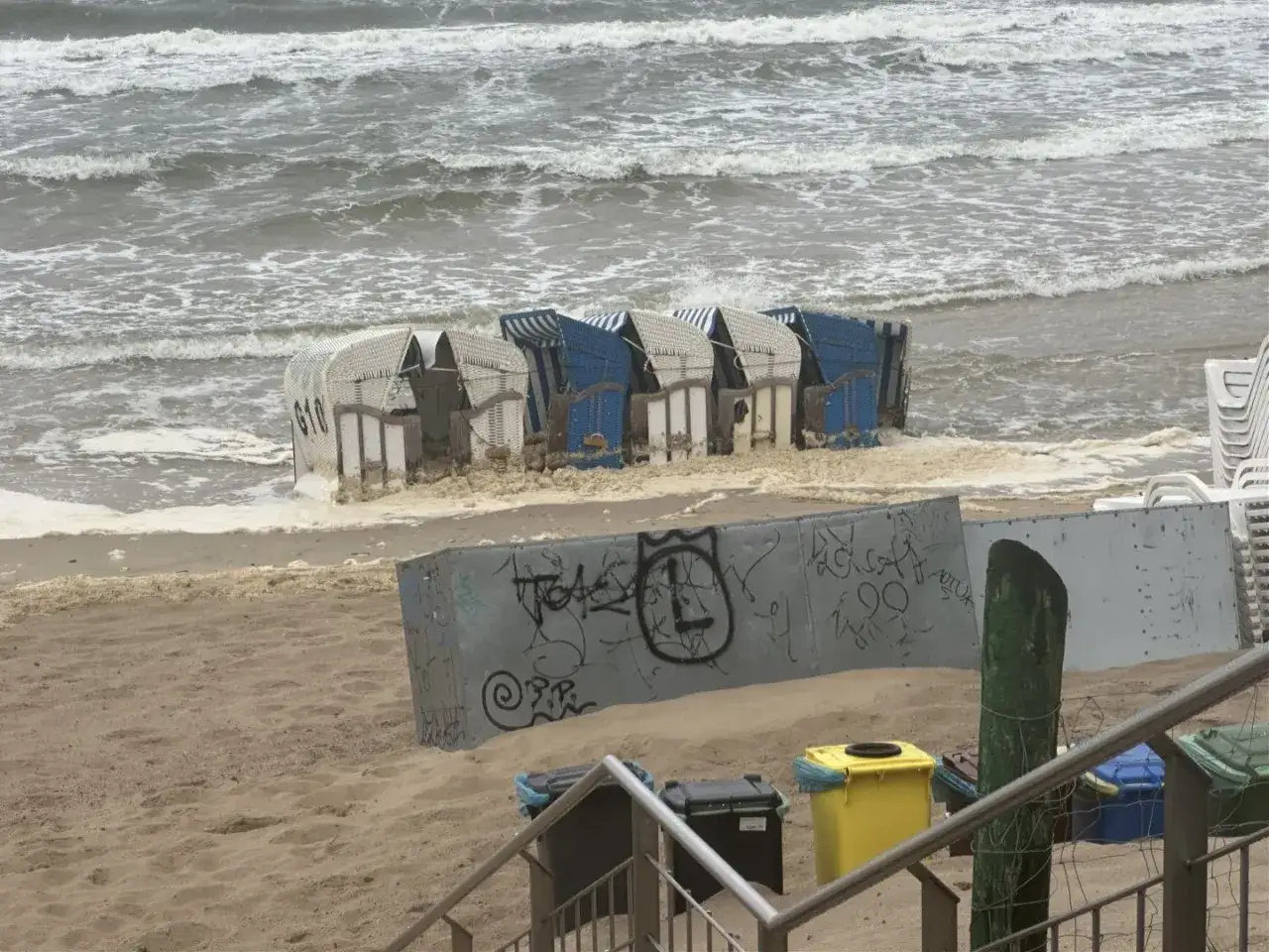 Fale zalewają plażowe budki, tworząc pianę. W tle widać wzburzone morze, a na piasku ślady po sztormie. To był trudny dzień dla miłośników jod nad morzem.