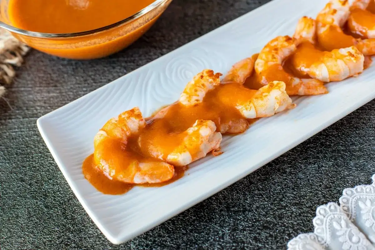 Camarones cubiertos con una cremosa salsa americana, servidos en una bandeja blanca.