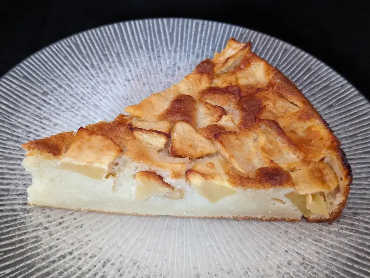 Une part de clafoutis aux pommes, comme dans le carnet de Julie, sur une assiette textur&eacute;e.