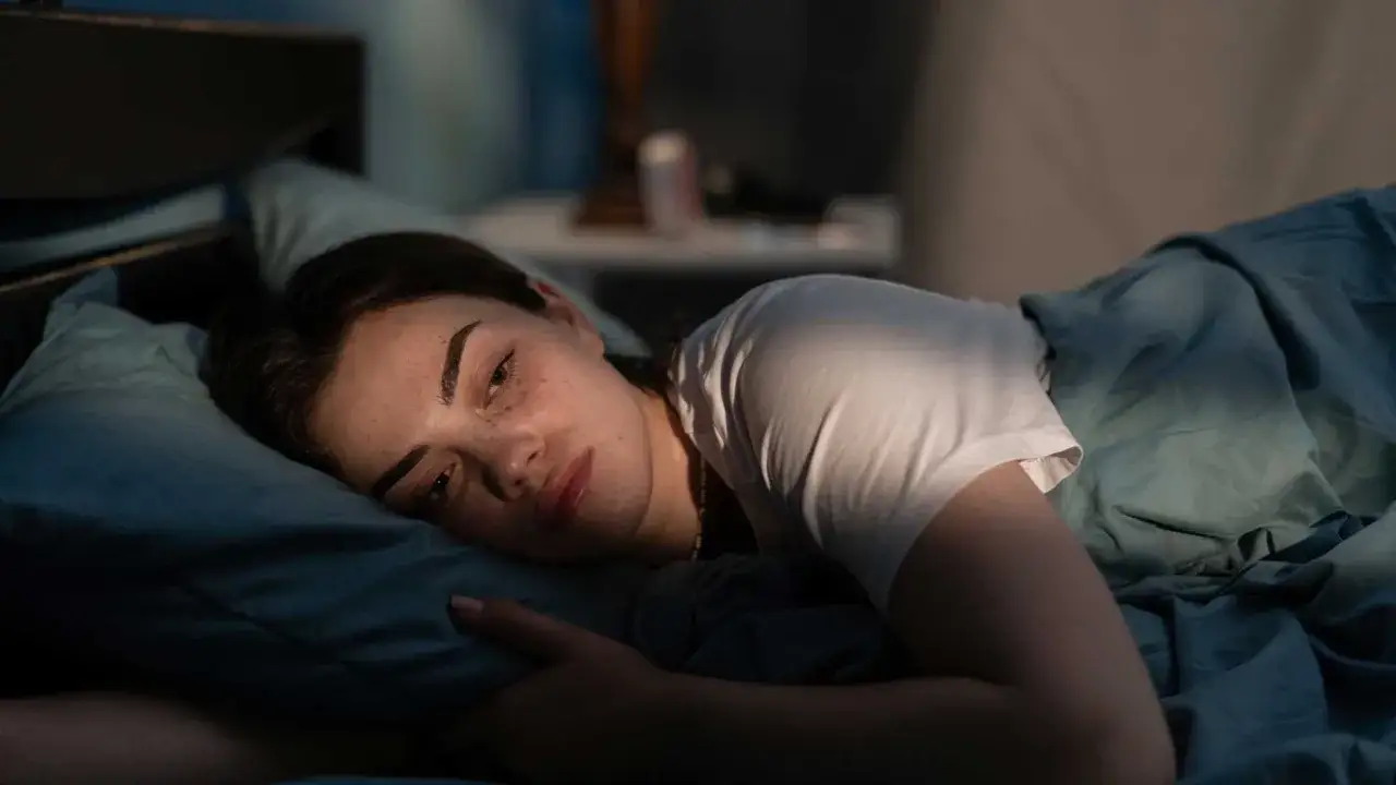 Ein junges Mädchen liegt im Bett, die Augen weit offen. Sie fragt sich, warum kann ich nicht einschlafen? Das Mondlicht fällt auf ihr Gesicht.