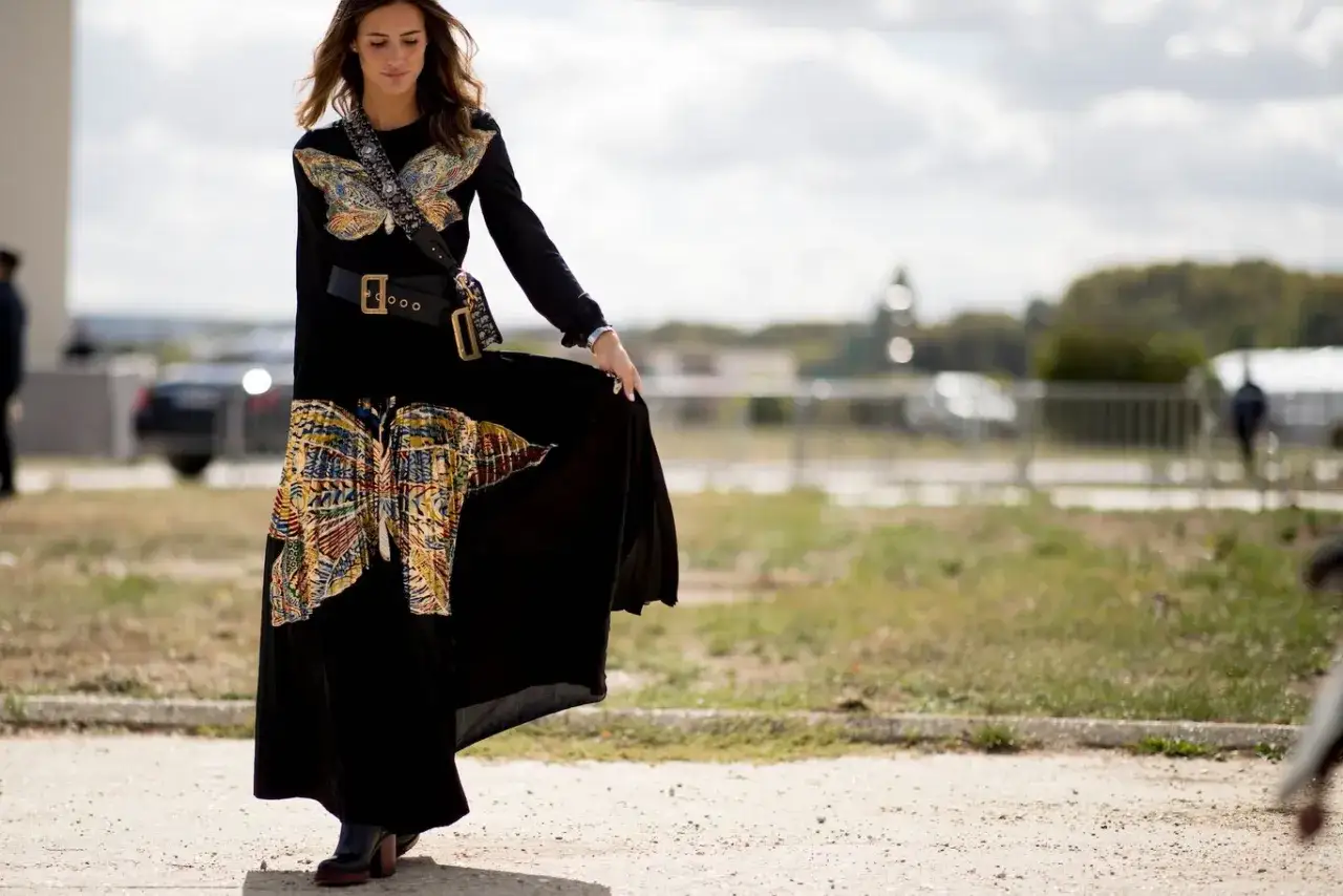 Mujer con vestido largo negro, estampado de mariposas y cinturón ancho. Un ejemplo de como llevar un vestido largo informal con estilo.