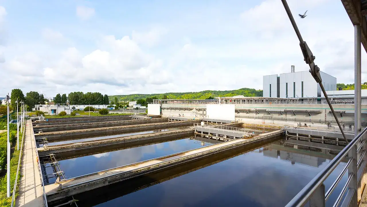 Station de traitement des eaux &agrave; Rouen, avec ses bassins de d&eacute;cantation et ses b&acirc;timents industriels sous un ciel nuageux.
