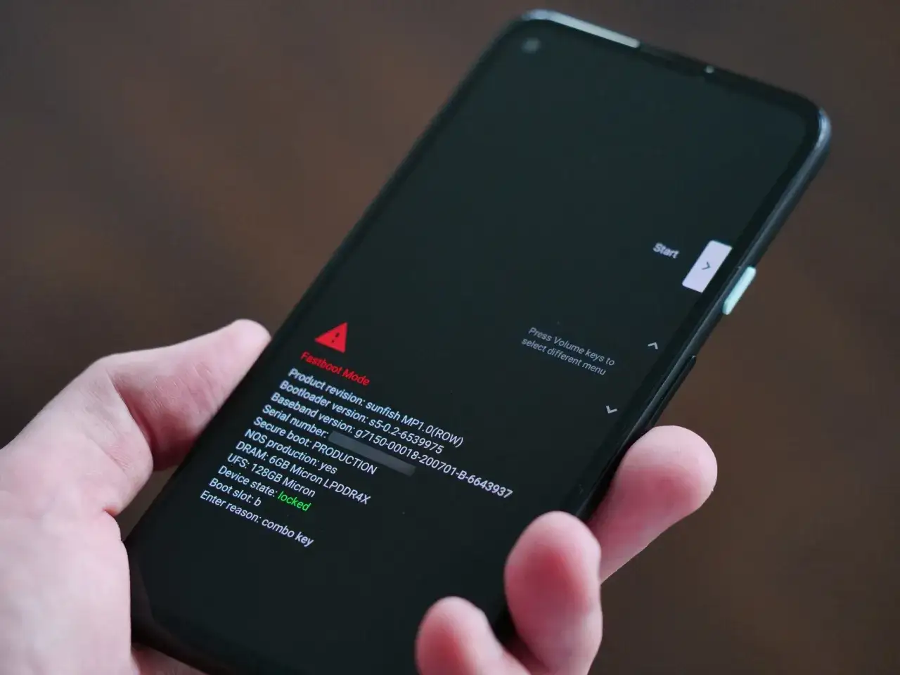 Dłoń trzyma smartfon z włączonym trybem **fastboot**. Na ekranie widoczne są informacje o wersji oprogramowania i stanie urządzenia.
