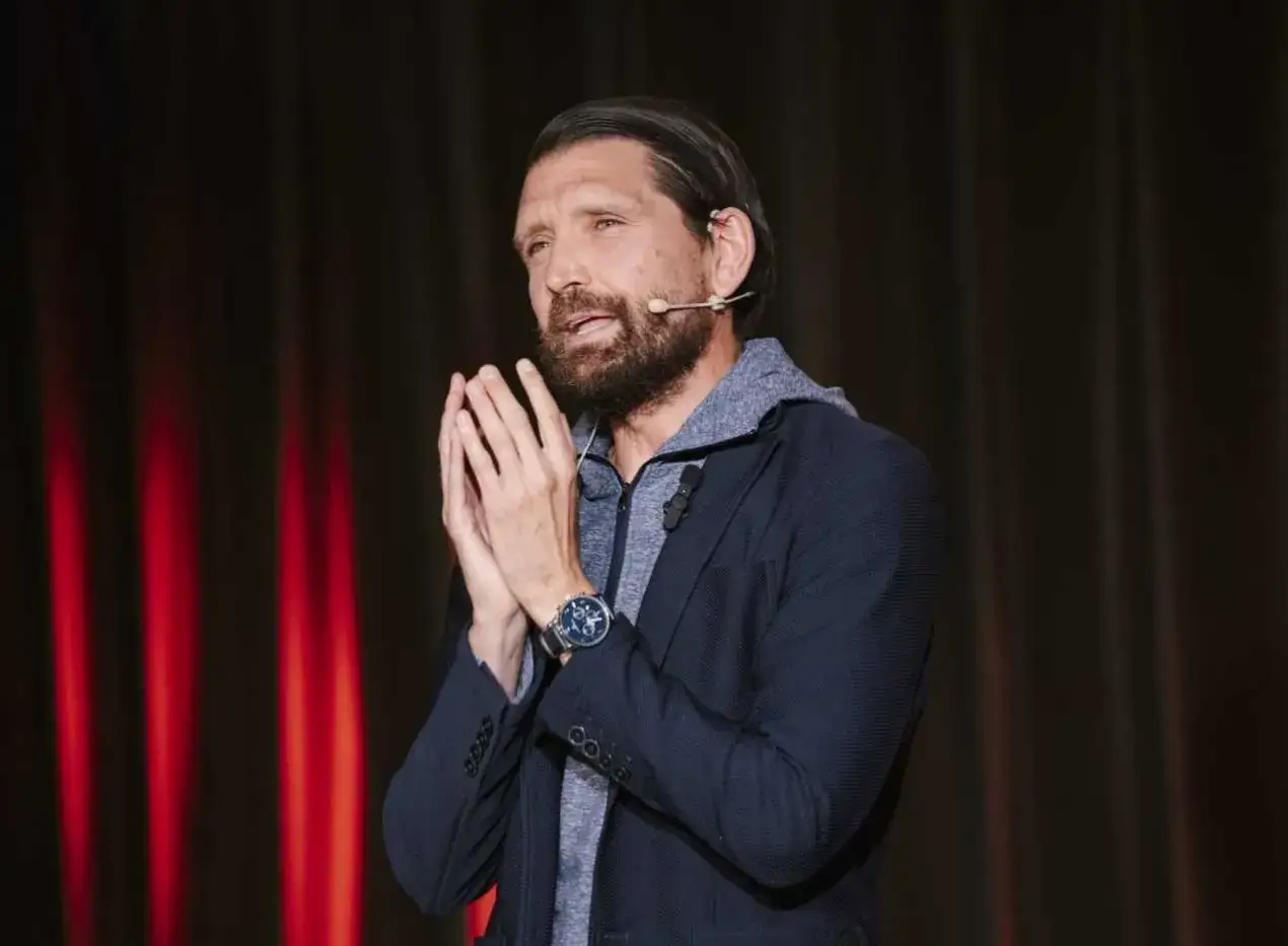 Peter Hyballa spricht mit gefalteten Händen vor einem roten Vorhang.