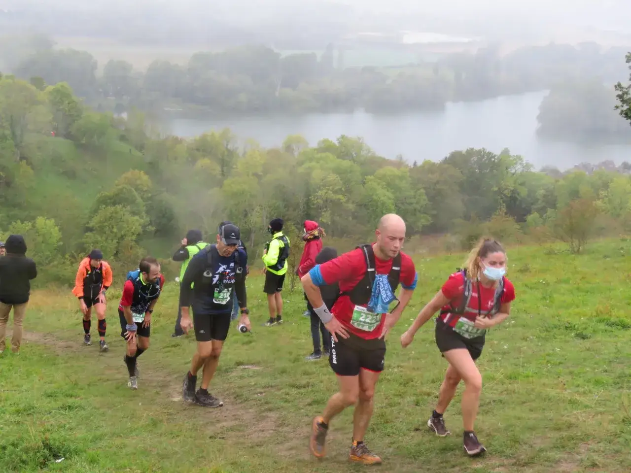 Coureurs en pleine ascension lors du trail des rois maudits, avec un lac brumeux en arri&egrave;re-plan.