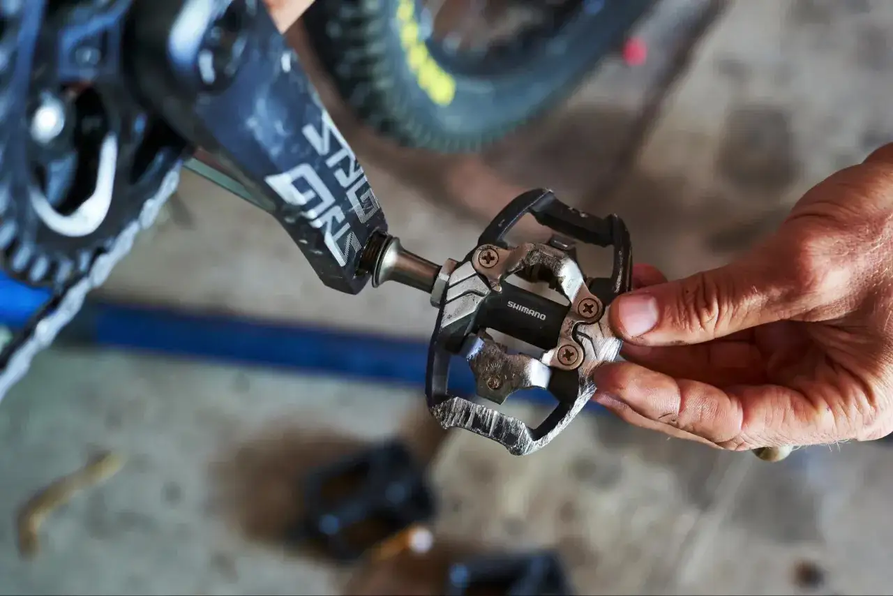 Dłoń trzyma pedał rowerowy Shimano, przygotowując ustawienie blok&oacute;w SPD.