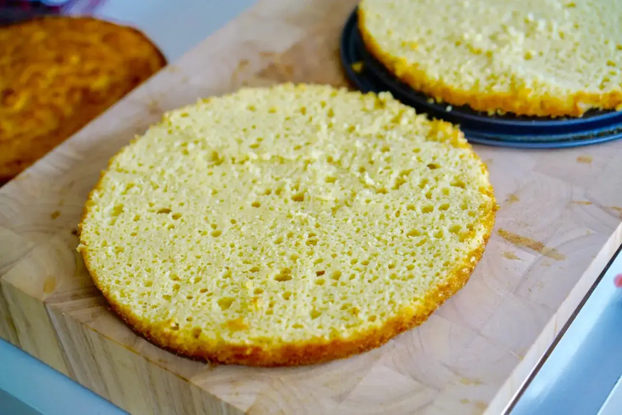 Två runda, fluffiga glutenfri tårtbotten ligger på en skärbräda. En ligger i en form, den andra bredvid.