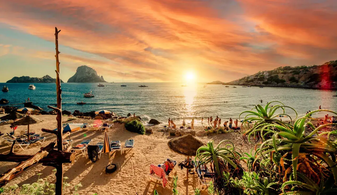 Un atardecer espectacular en Ibiza, con el sol ti&ntilde;endo el cielo de naranja sobre el mar y la silueta de Es Vedr&agrave;. Un lugar perfecto donde ver el atardecer en Ibiza.