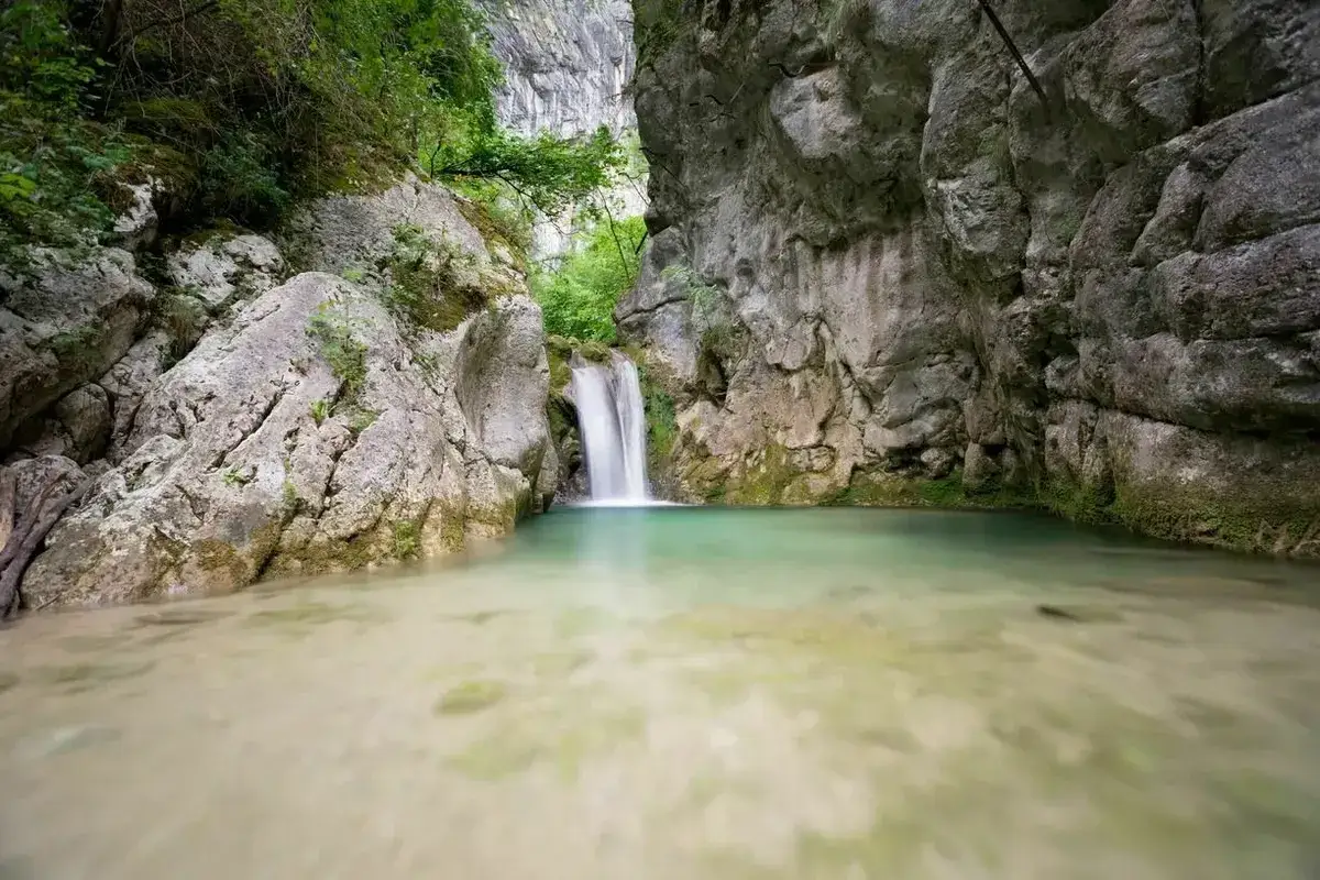 Cascade d'eau tombant dans un bassin turquoise au c&oelig;ur de la gorge du Nan, entour&eacute;e de falaises rocheuses et de v&eacute;g&eacute;tation luxuriante.