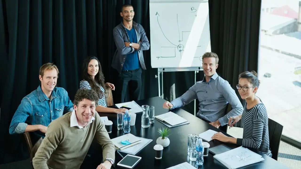 En grupp aff&auml;rsfolk diskuterar ledningsgruppens uppdrag vid ett m&ouml;tesbord. En whiteboard med diagram syns i bakgrunden.