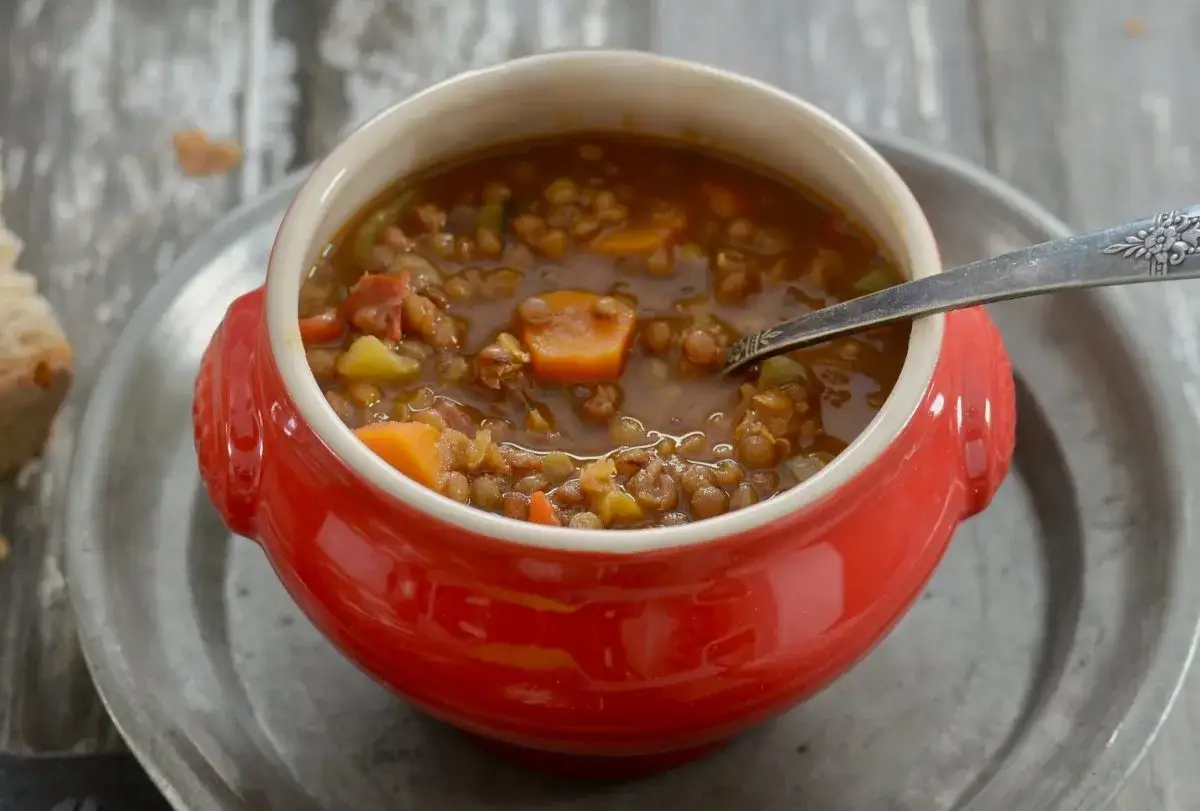 Un cuenco rojo con lentejas estofadas estilo Argui&ntilde;ano, llenas de verduras y trocitos de chorizo.