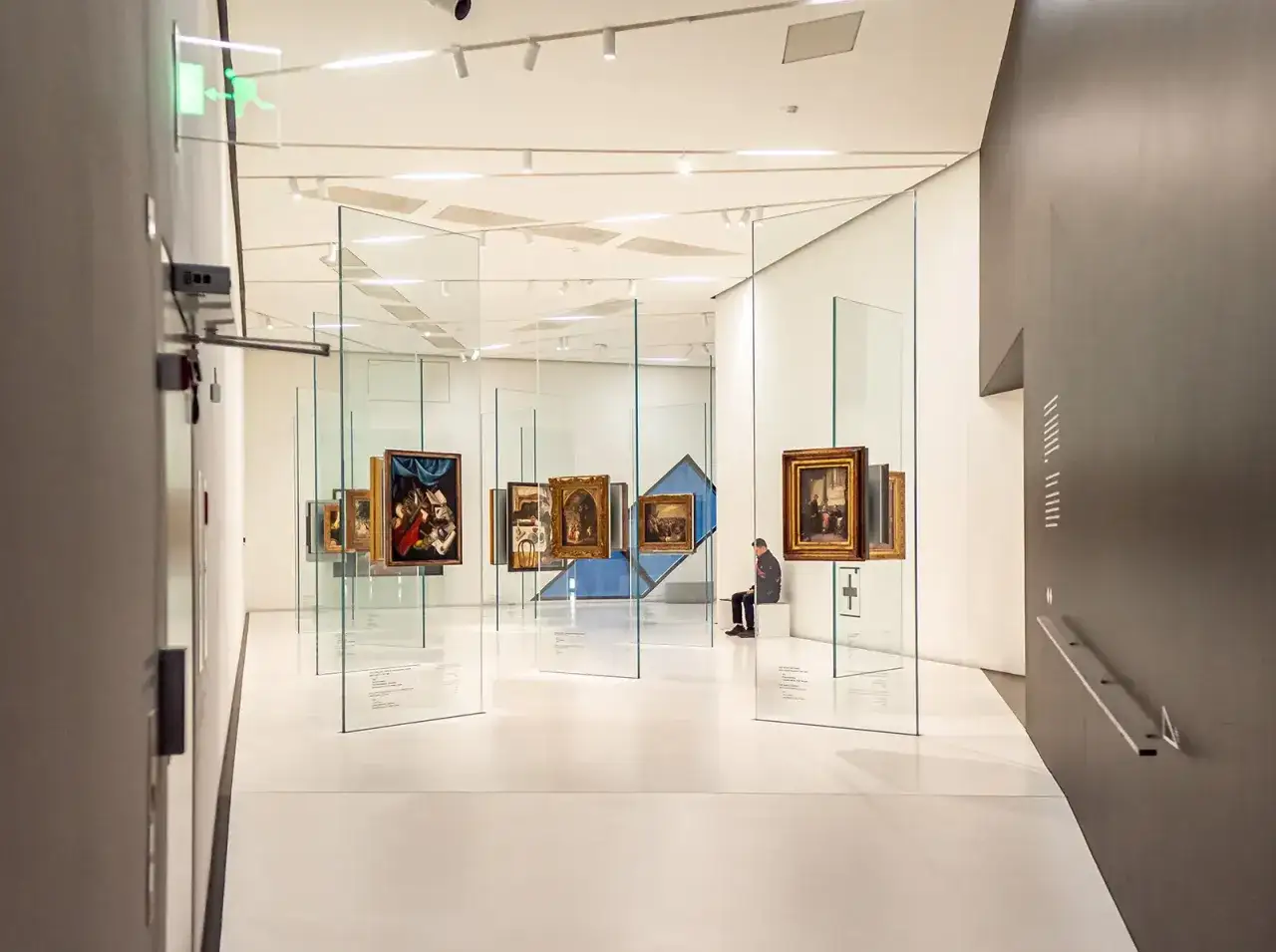 Wnętrze muzeum żydowskiego w Berlinie. Obrazy w złotych ramach wiszą na szklanych panelach.
