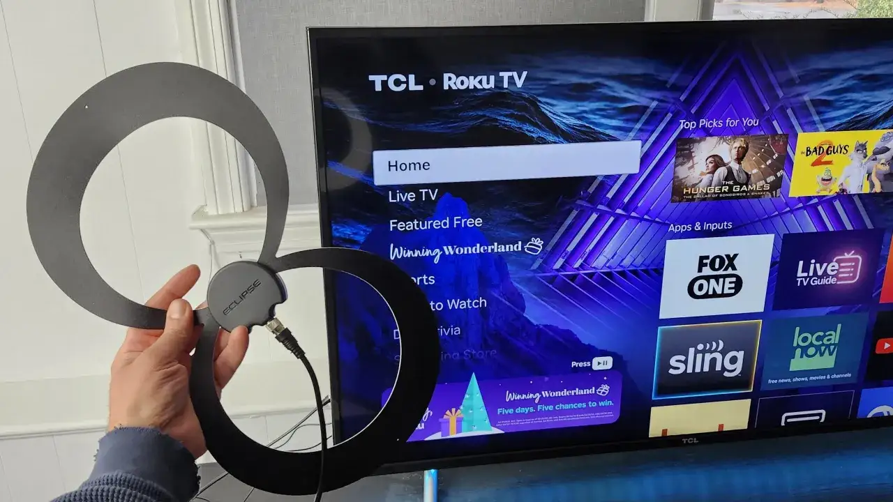 Czy bez anteny można oglądać telewizję? Ręka trzyma czarną antenę przed ekranem telewizora TCL Roku TV, na którym widać menu 