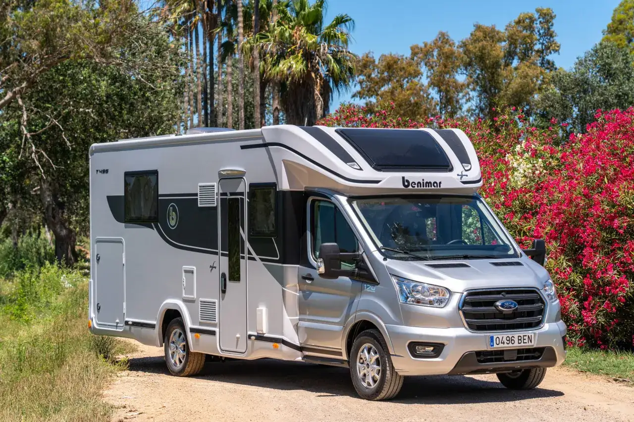 Kamper Ford Benimar T496 zaparkowany na drodze wśród zieleni i kwitnących krzewów.