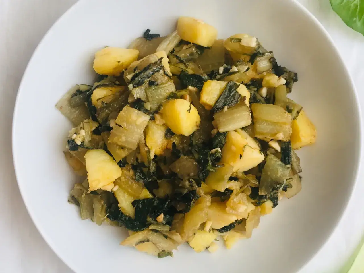 Un plato de acelgas con patatas, cocinado con ajo y especias, servido en un cuenco blanco.
