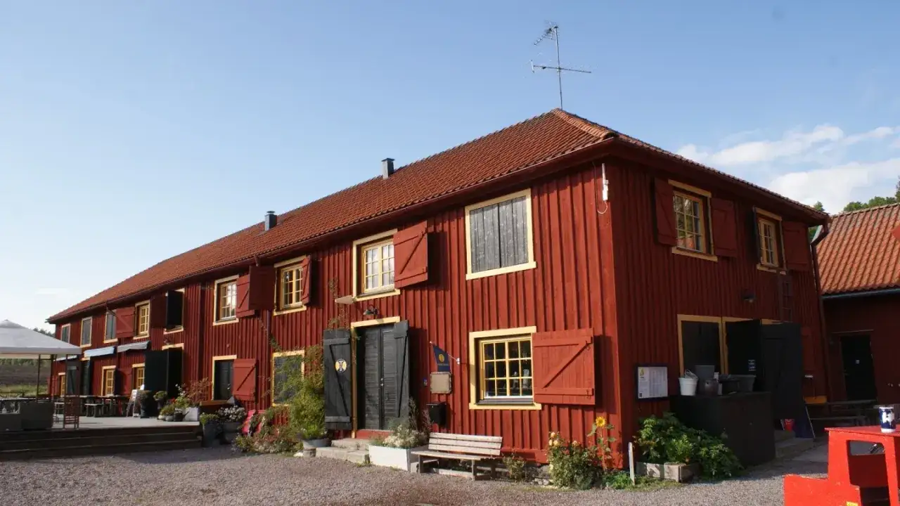 Rött trähus med gula fönsterdetaljer och röda fönsterluckor. Sjötorp vandrarhem välkomnar med sin charmiga fasad.