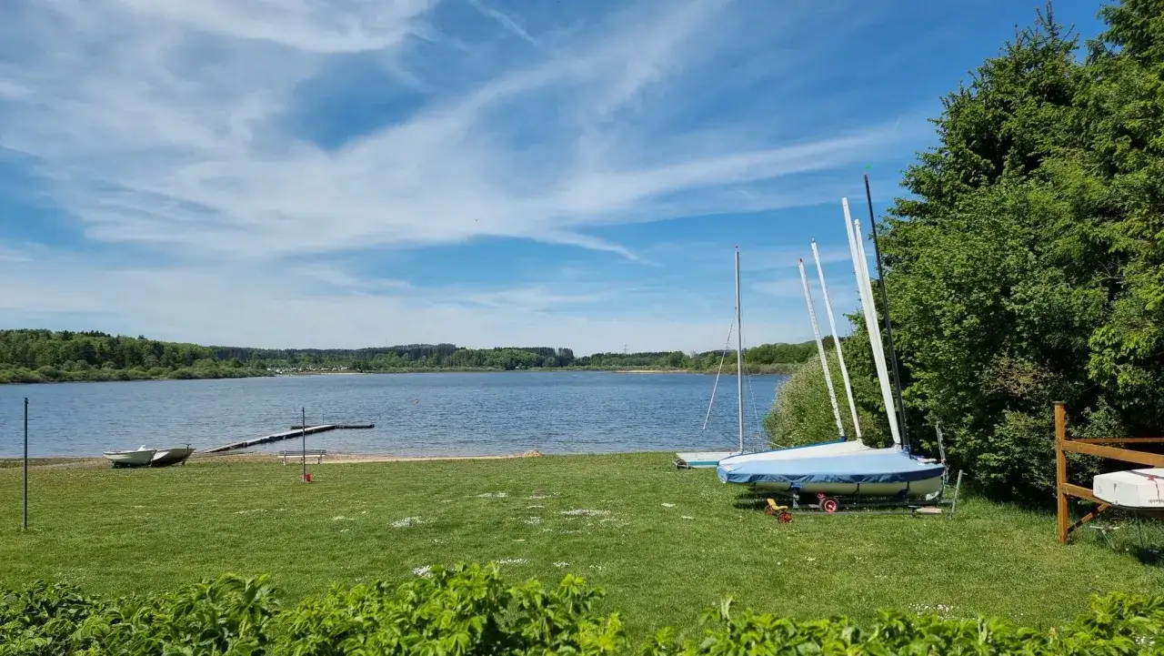 Segelboote am Ufer der Krombachtalsperre, bereit f&uuml;r den Rundweg. Ein sonniger Tag mit blauem Himmel und Wolken.
