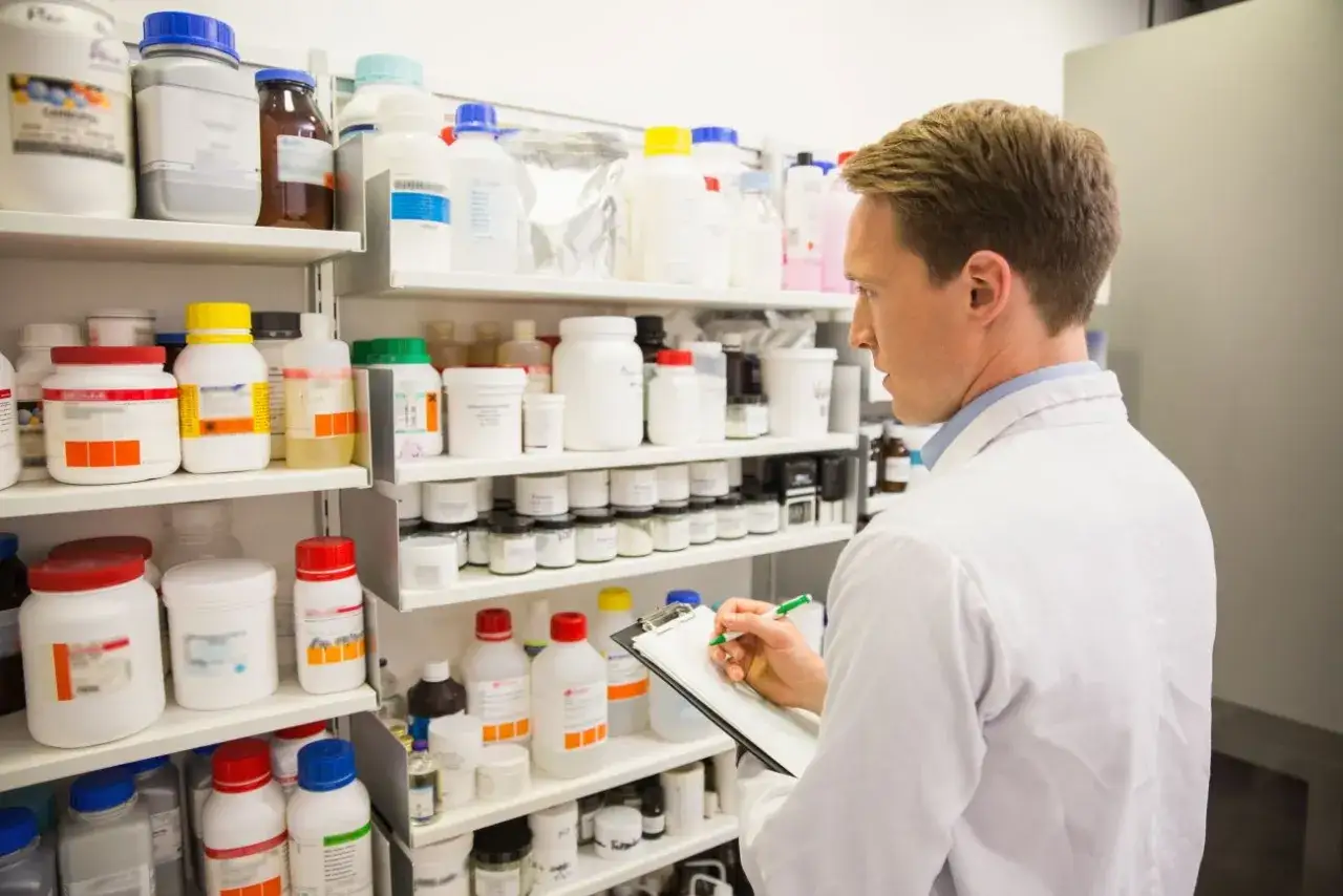 Farmaceuta sprawdza zapasy, w tym amlodypinę, na półkach pełnych leków i odczynników.