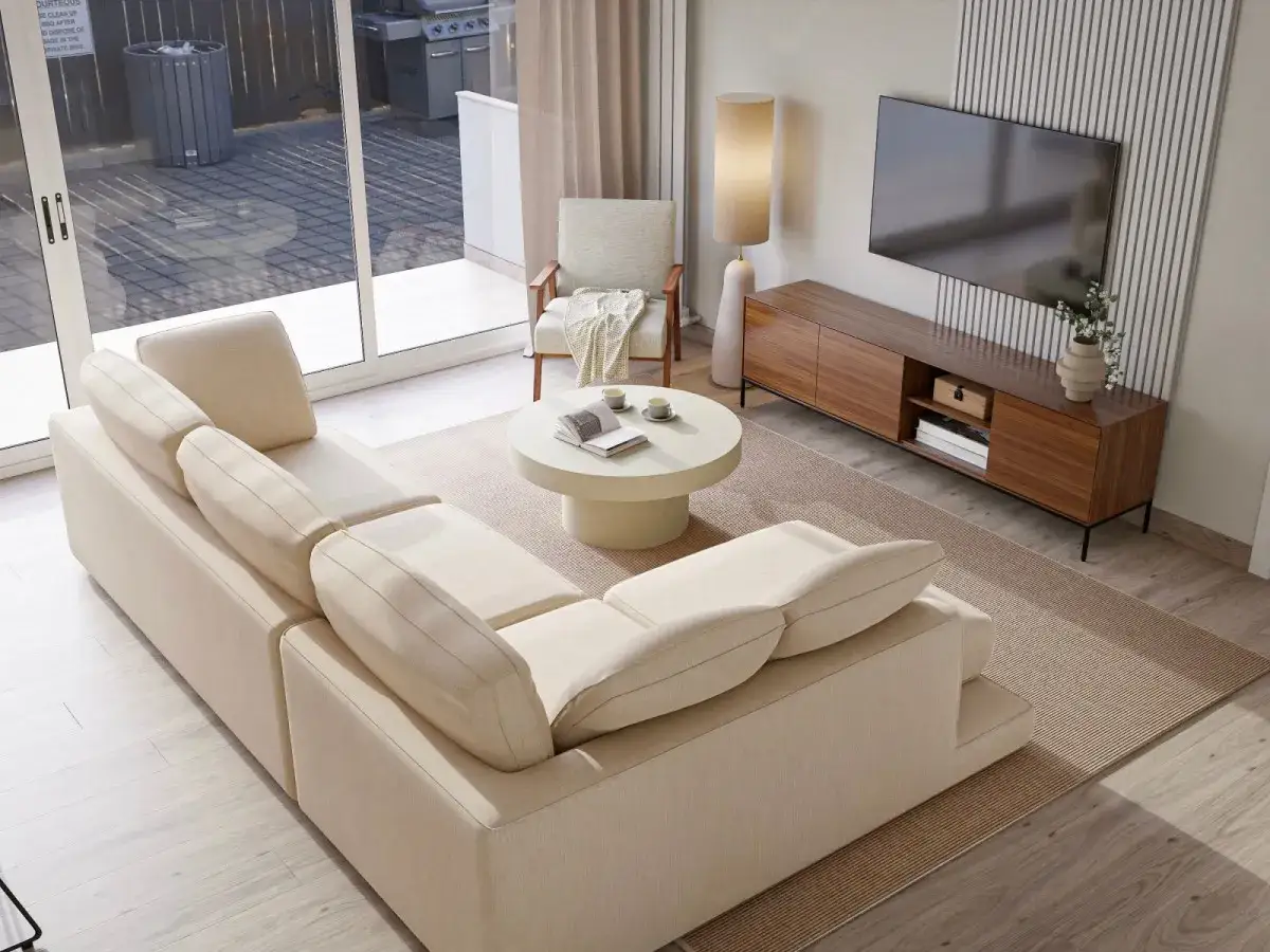 Sofá modular color crema, ideal como color de sofá para paredes blancas. Mesa de centro redonda, alfombra beige y mueble de TV de madera.