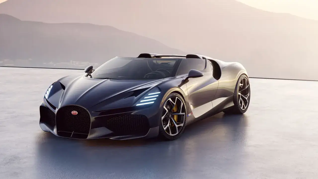 Dunkelblauer Bugatti Mistral Roadster steht auf einer Betonfl&auml;che vor einer Bergkulisse.