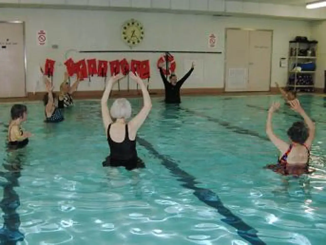 Grupa seniorów ćwiczy w basenie, wykonując ruchy ramion. To przykład aktywnego multisport senior.