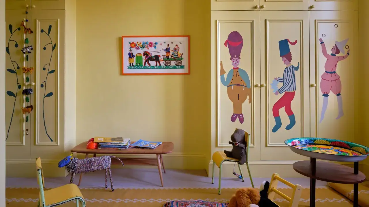 Ein fröhliches Kinderzimmer mit gelben Wänden und Schränken, die mit bunten Motiven bemalt sind. Ein Bild mit einer Pferdekutsche und Spielzeugtiere schmücken den Raum.