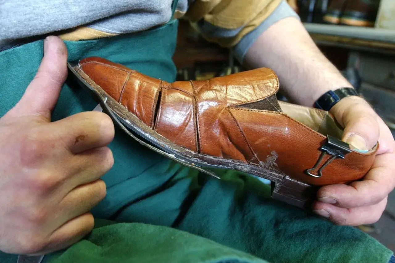 Un cordonnier examine une chaussure en cuir marron, démontrant qu'il est possible de ressemeler des baskets.