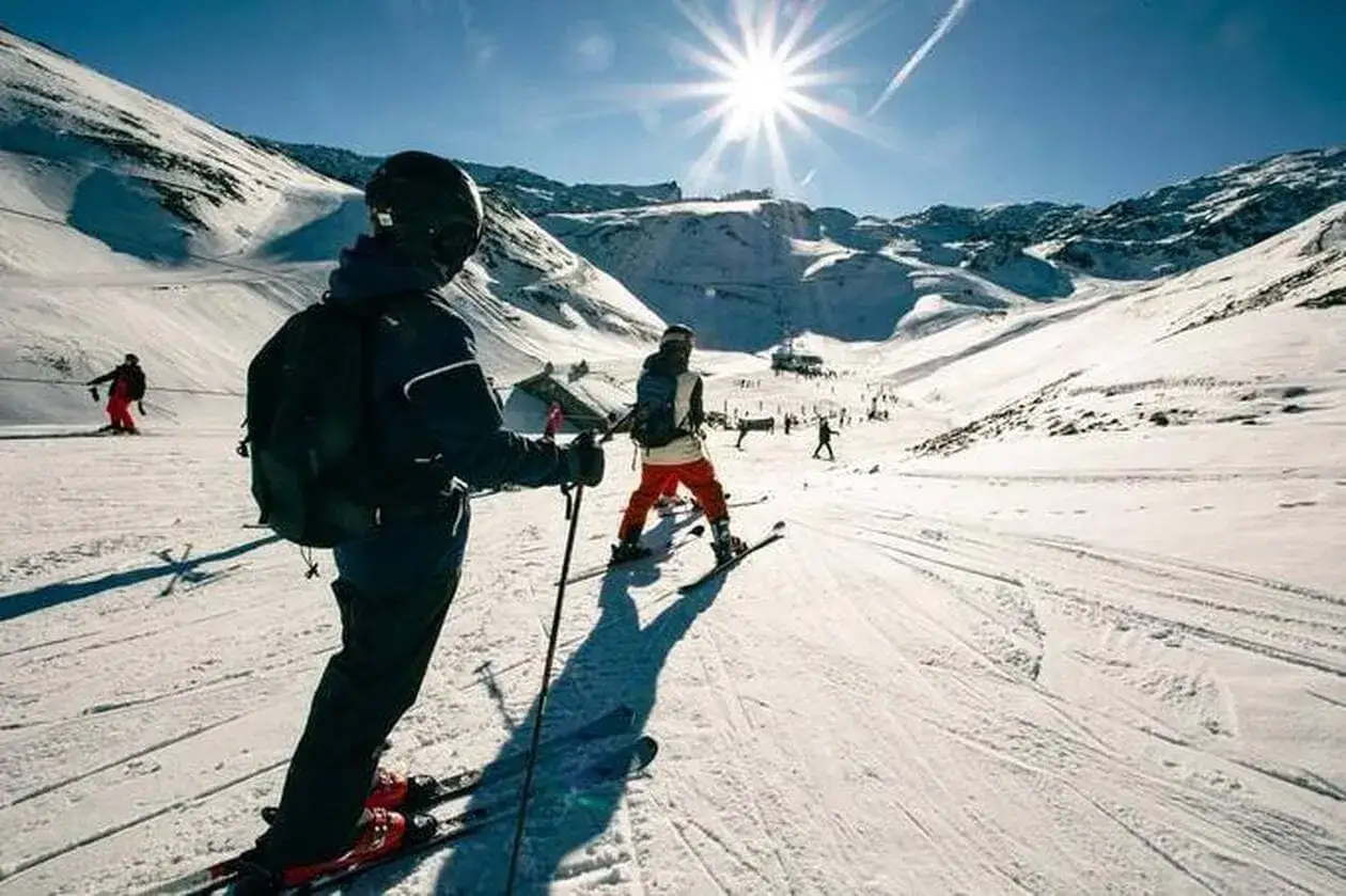Des skieurs profitent d'une journée ensoleillée pour pratiquer le sport alpin sur une piste enneigée, avec des montagnes majestueuses en arrière-plan.